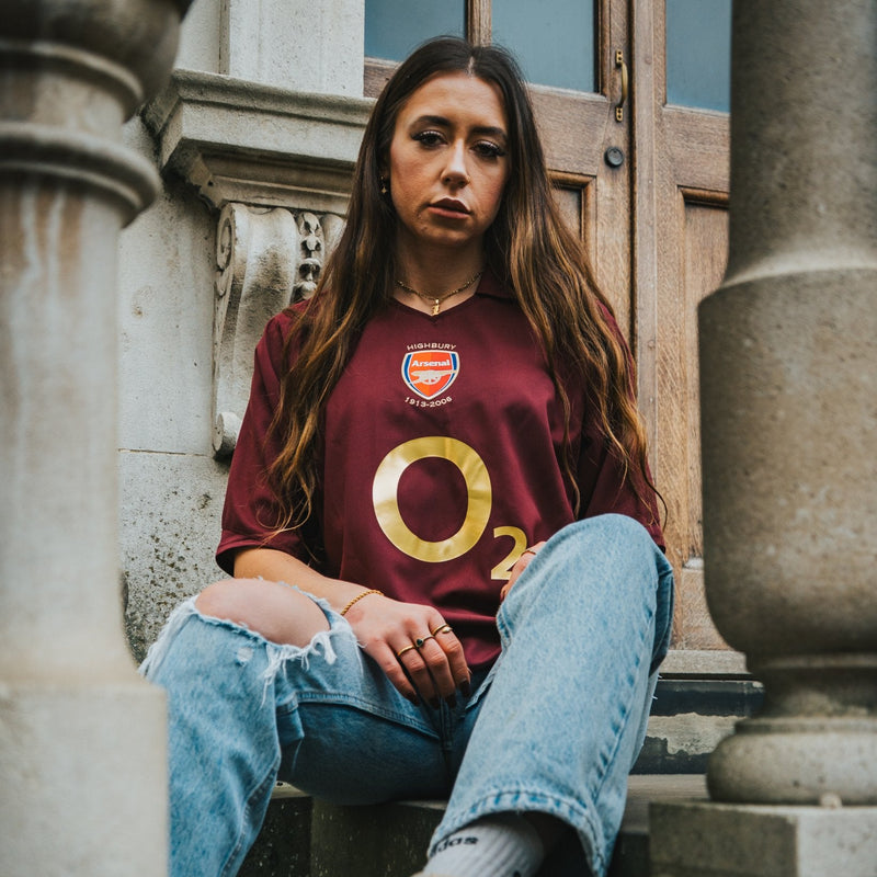 Person wearing a maroon sports jersey with a logo, sitting on stone steps.