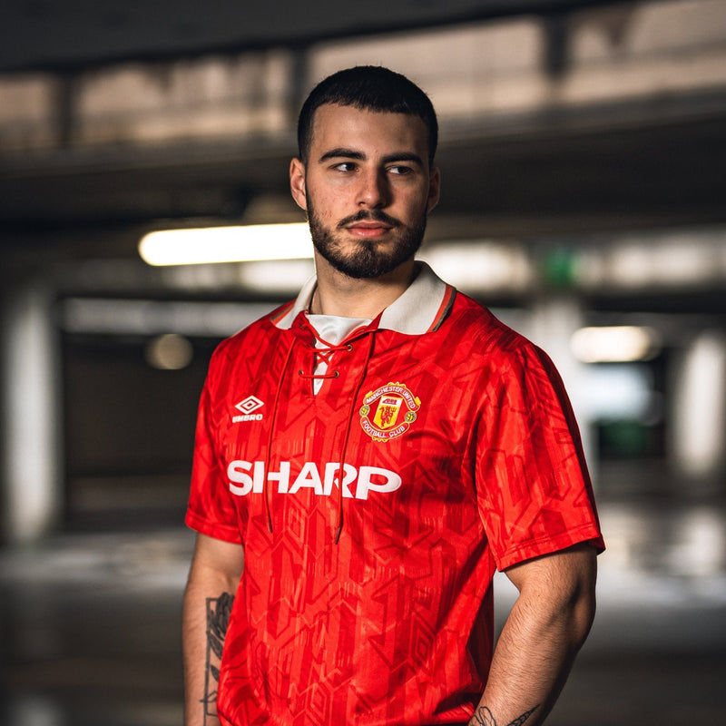 Man wearing a red Manchester United jersey with 'Sharp' logo in an indoor setting