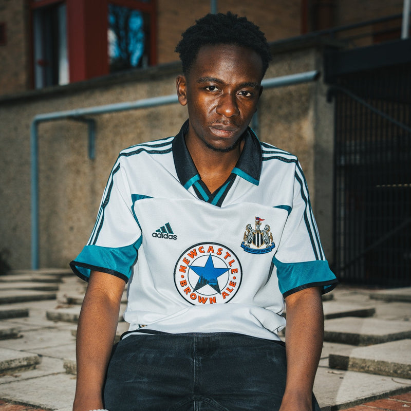 Person wearing a Newcastle United football jersey sitting on steps.