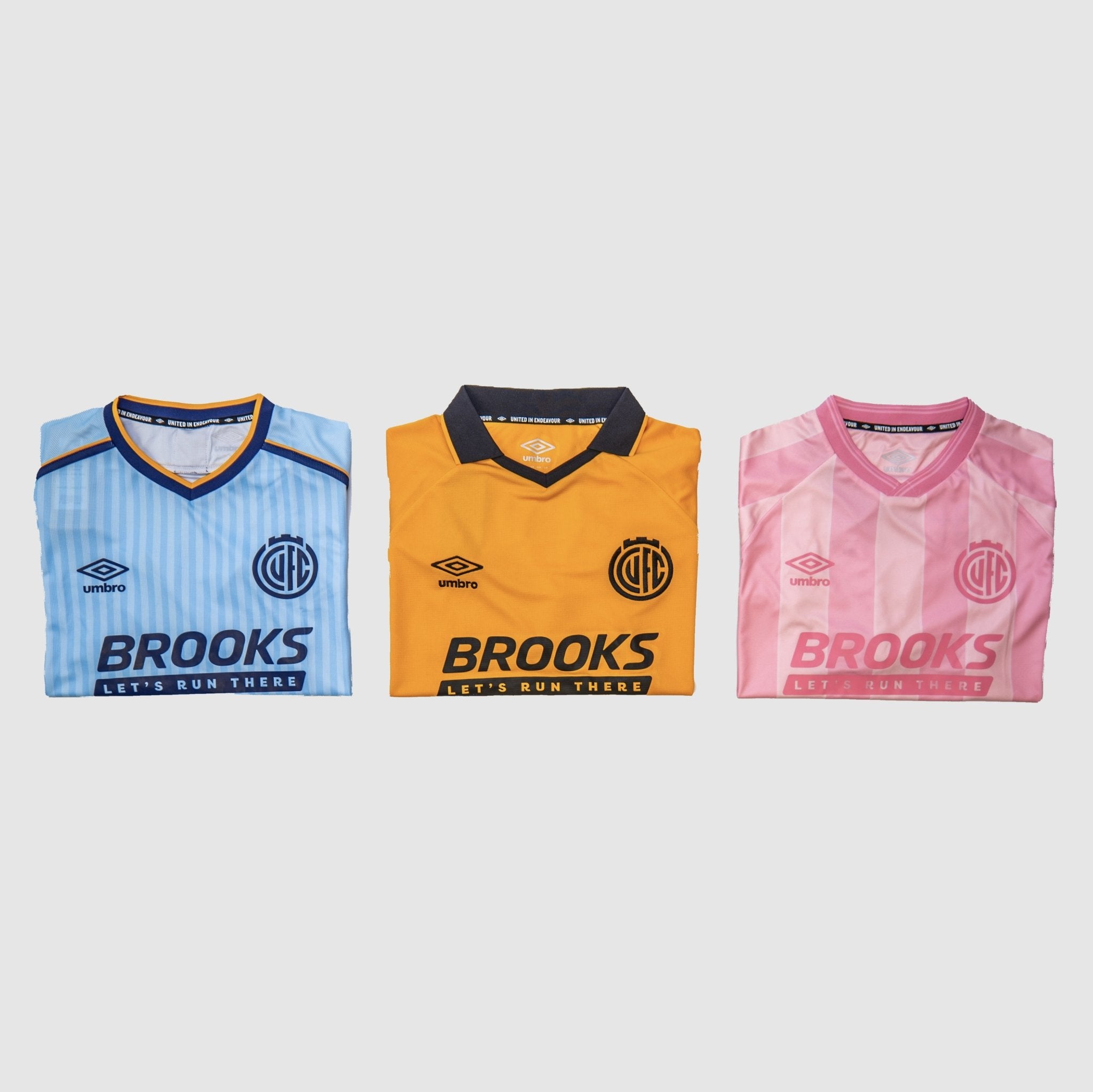 Three folded vintage-style football jerseys displayed side by side on a light gray background: a light blue striped jersey with navy trim, an orange-yellow jersey with a dark collar, and a pink vertically striped jersey with pink trim. Each jersey shows the Brooks sponsor logo and a club crest.